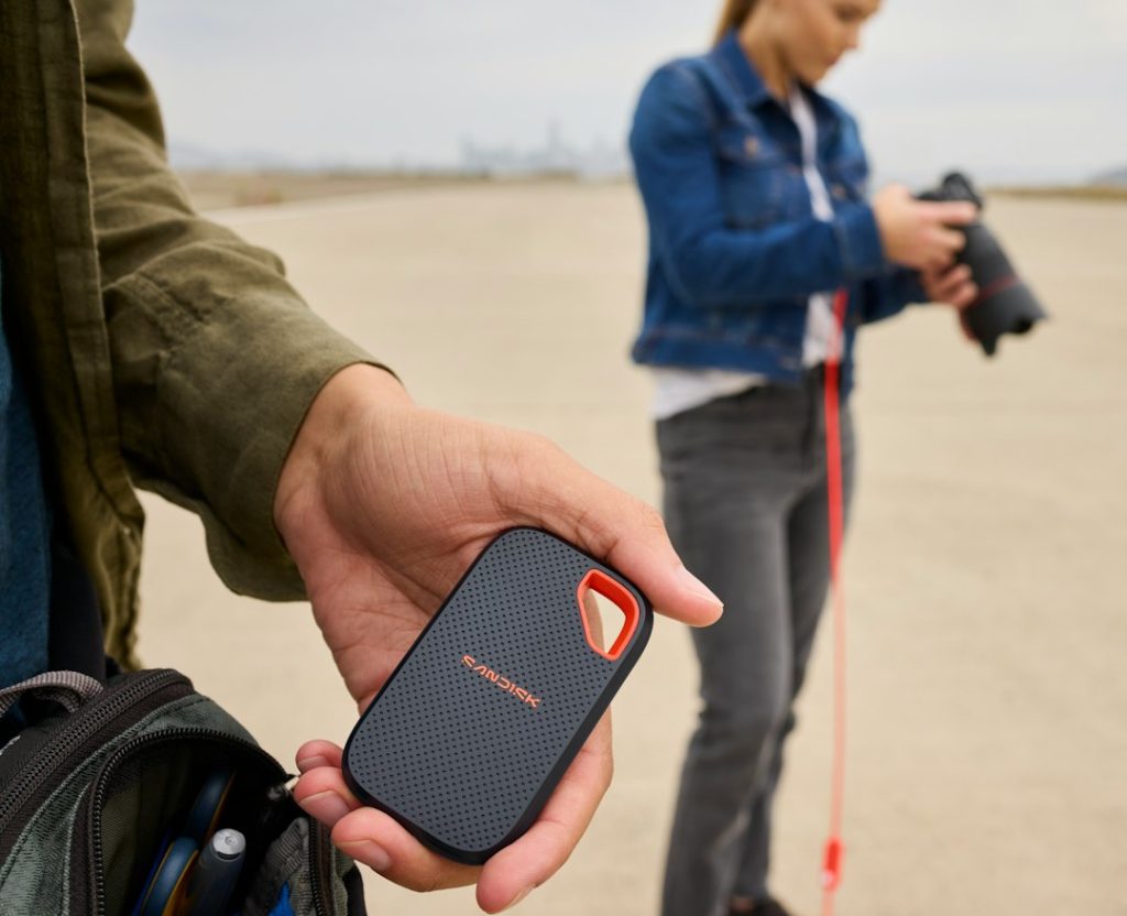 A hand holds a portable ssd, another person uses camera